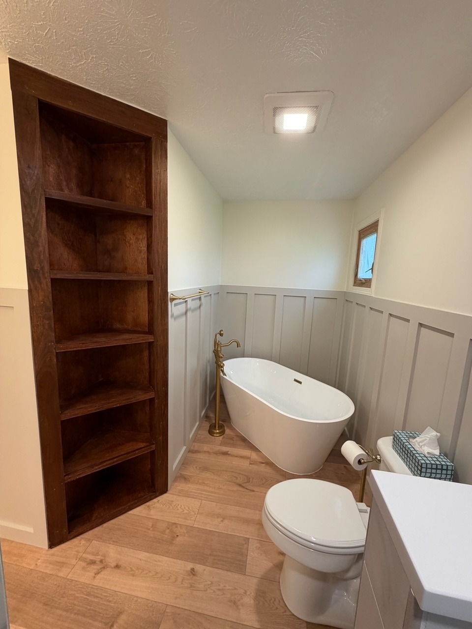 Freestanding bathtub beside custom dark wood shelving and paneled walls
