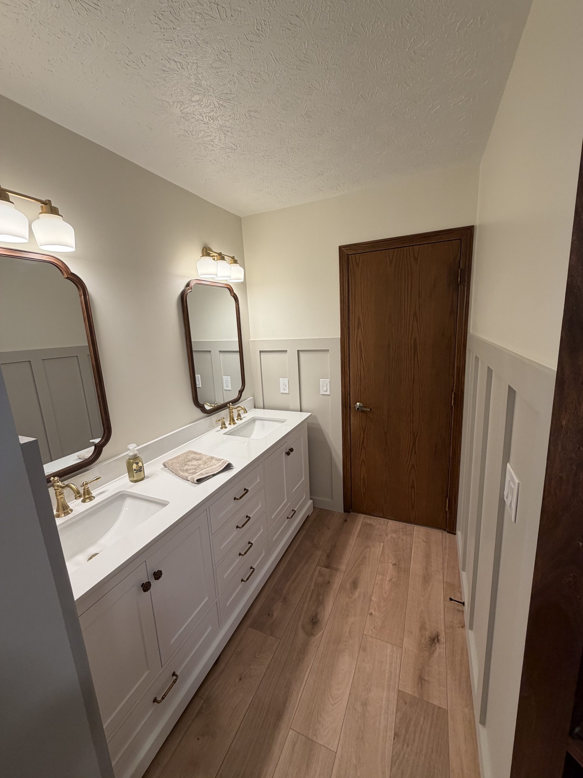 Double vanity with brass faucets, framed mirrors and wood-look flooring