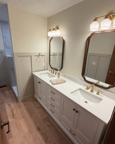 Remodeled bathroom with double sink vanity, framed mirrors, brass fixtures and wood-look floor